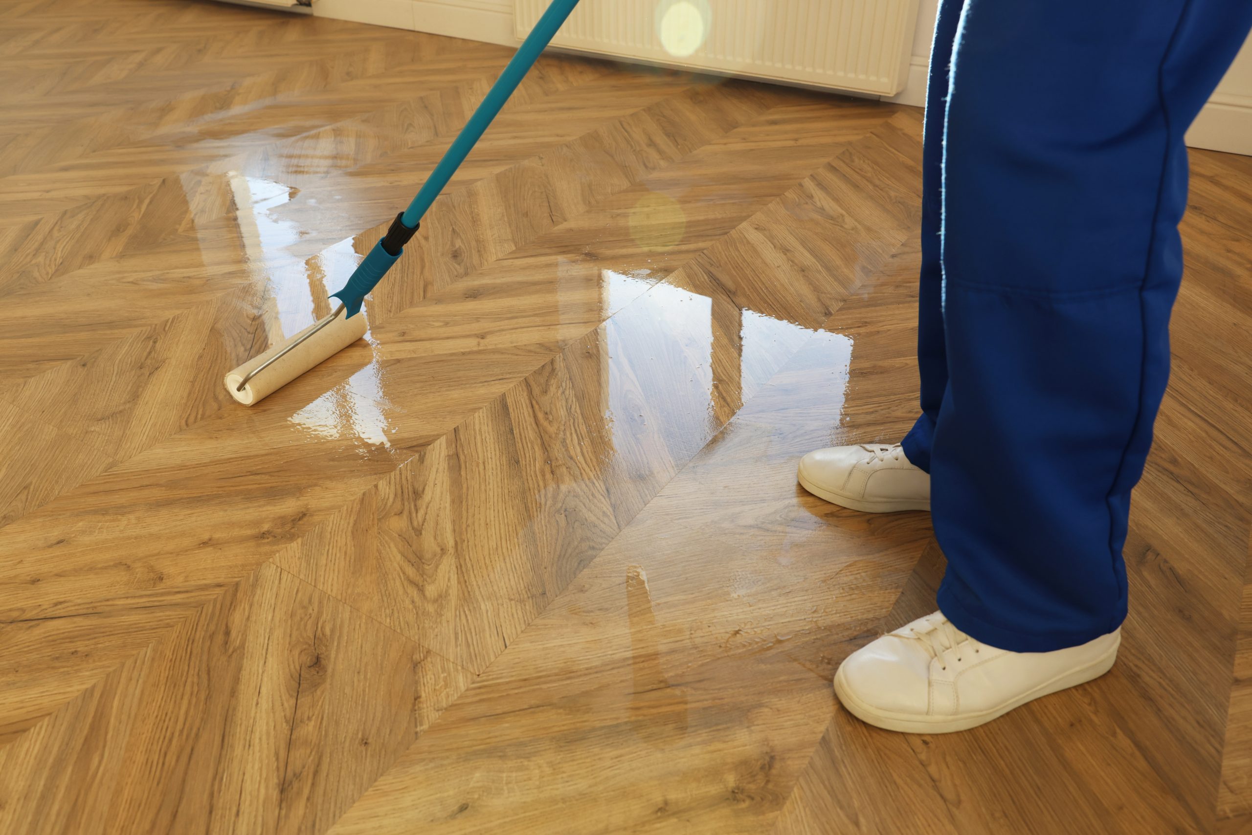 Parquet Floor Sanding in Finchley with technician applying clear finish to an oak chevron parquet floor after sanding.
