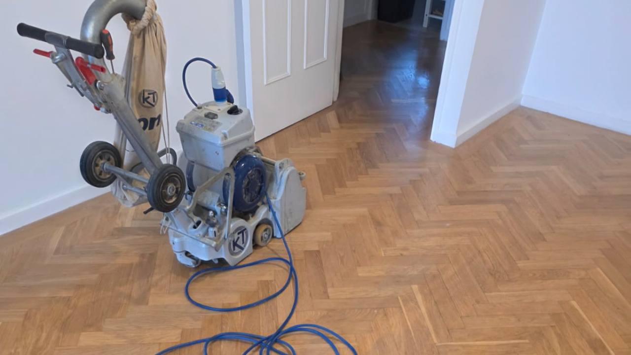 Parquet Floor Sanding in Finchley with professional belt sander on an oak herringbone parquet floor, showing a freshly sanded smooth surface.