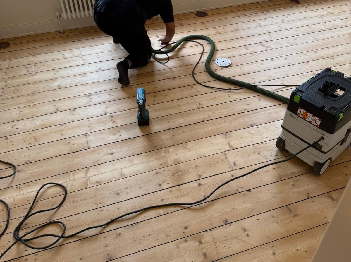 Wood Floor Sanding in Finchley – technician carrying out dust-free finishing on softwood pine floorboards in a living room.