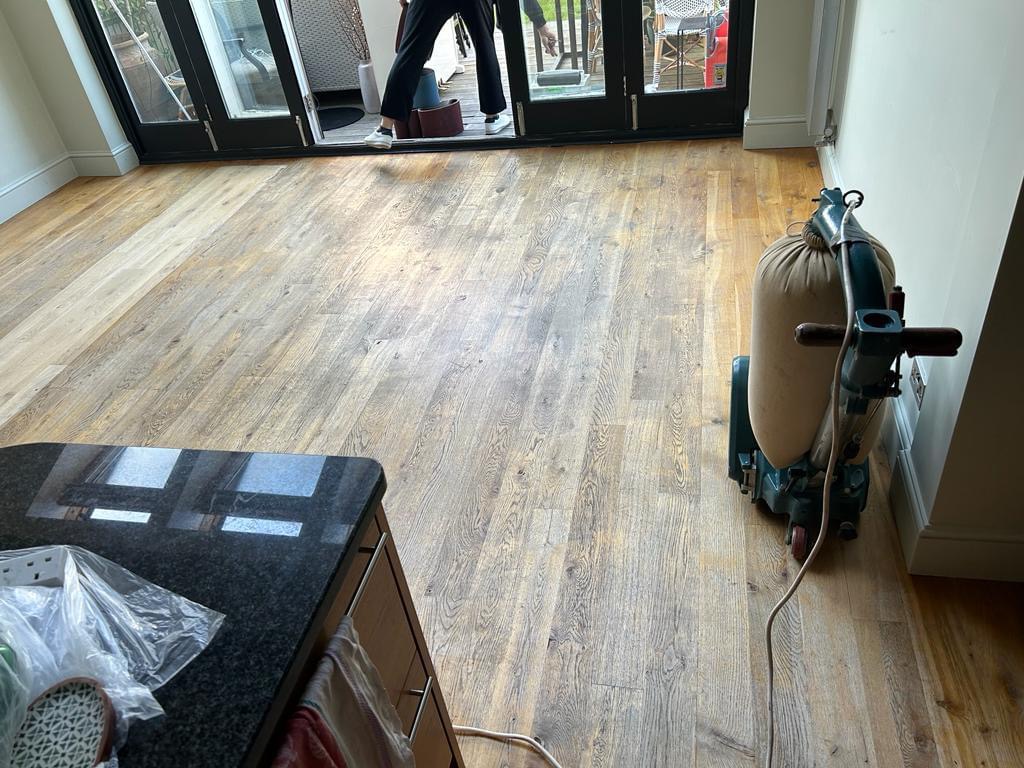 Wood Floor Sanding in Finchley – engineered oak kitchen diner floor in preparation, with a sanding machine positioned on the worn wooden boards near patio doors.