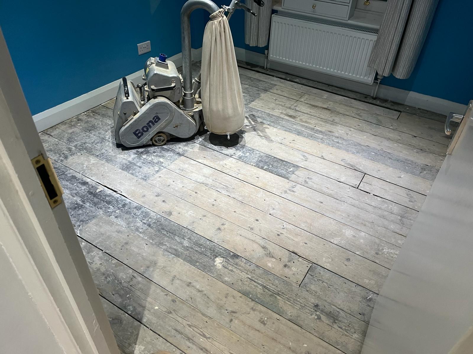 Wood Floor Sanding in Finchley – original bedroom pine floorboards in progress with a Bona sanding machine on the grey, worn wooden boards.