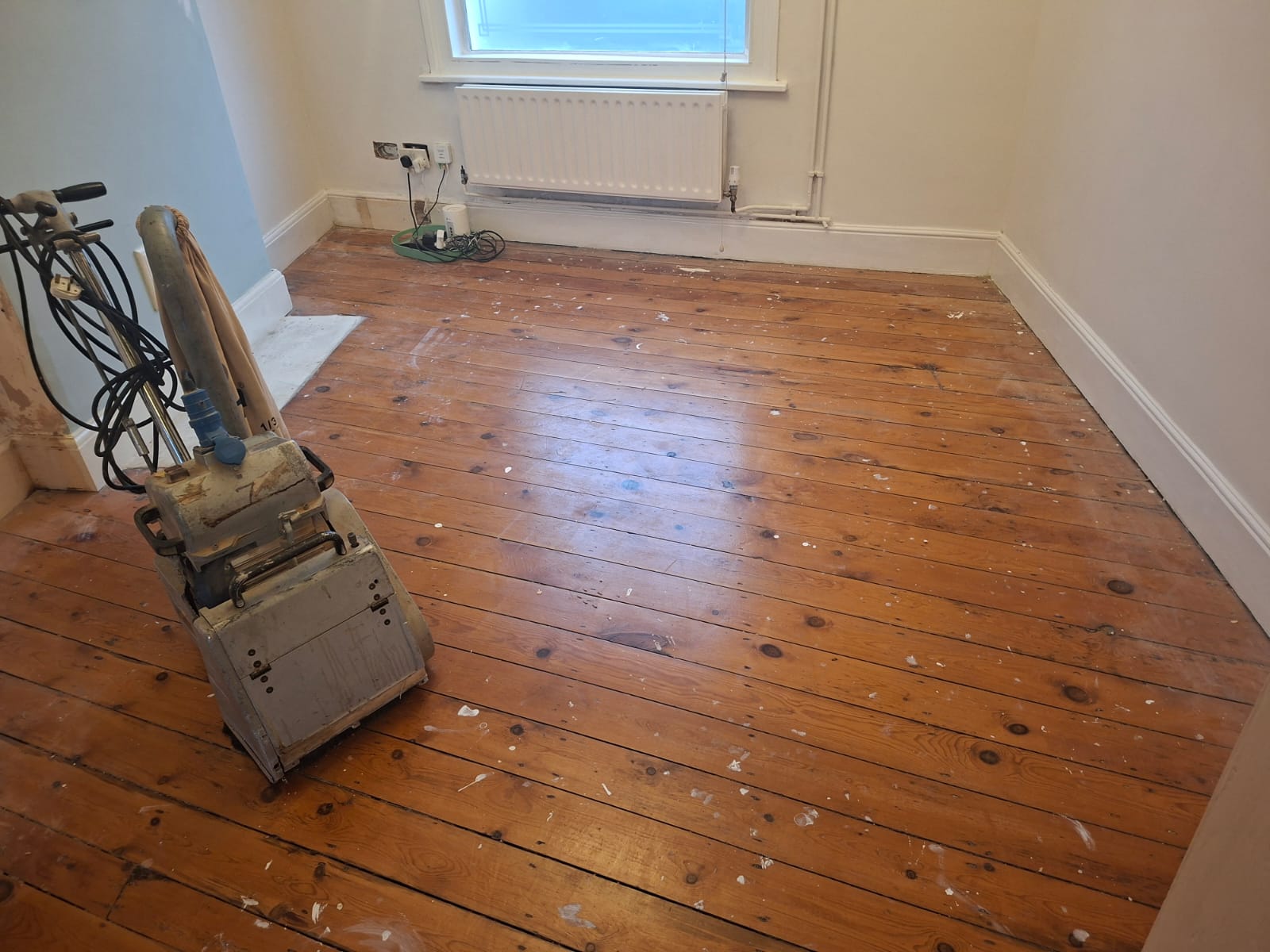 Wood Floor Sanding in Finchley – original pine floorboards in a bedroom with paint splashes and sanding machine ready for restoration.