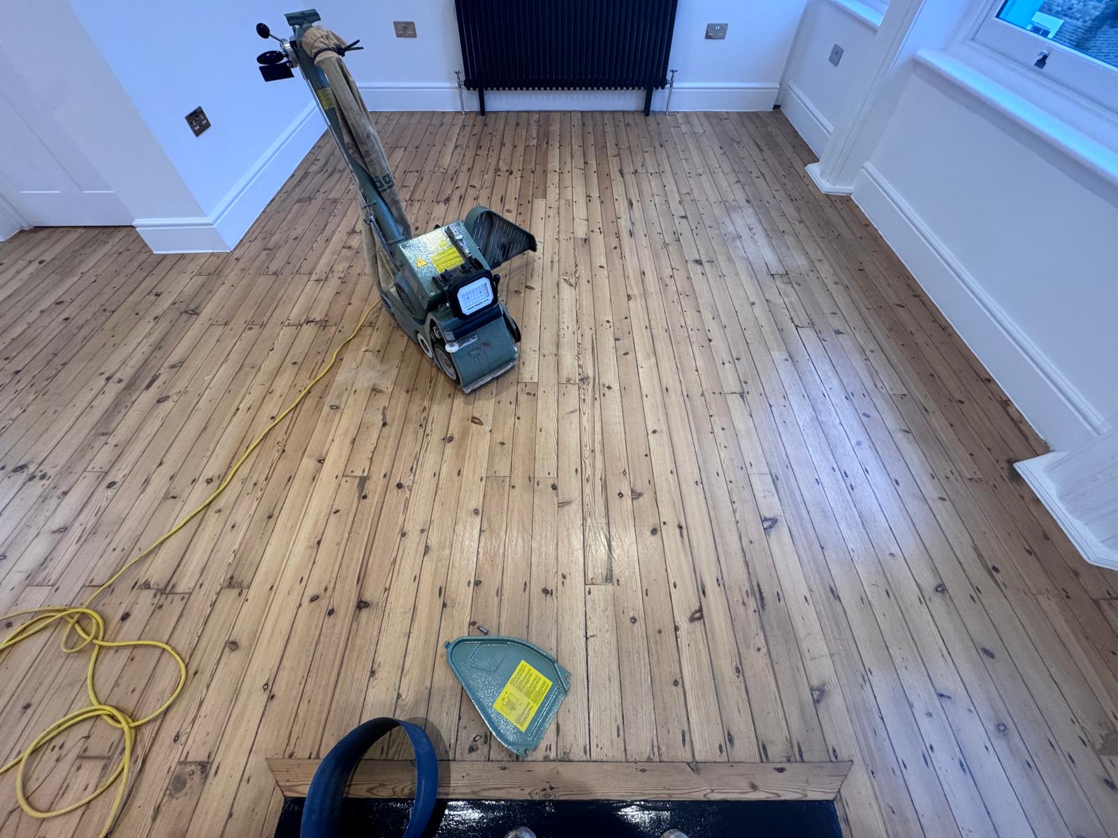 Wood Floor Sanding in Finchley – living room with softwood pine floorboards freshly sanded using a professional belt sander, showing a smooth, even wooden surface ready for finishing.